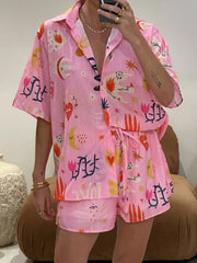 Pink co-ord set with short sleeves, button front, and drawstring shorts. Features a celestial and floral print.