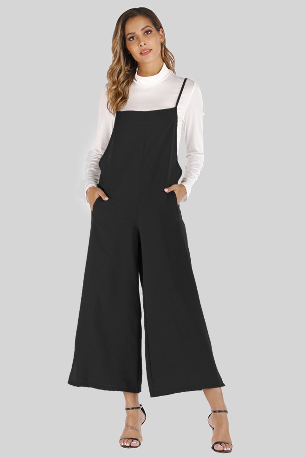 Black culotte overalls with slender straps and wide legs, styled with a white turtleneck.