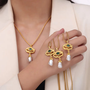 Gold botanical pearl drop pendant necklace with green stone detail.