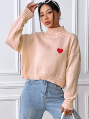 Apricot cropped turtleneck knit sweater with embroidered red heart detail.