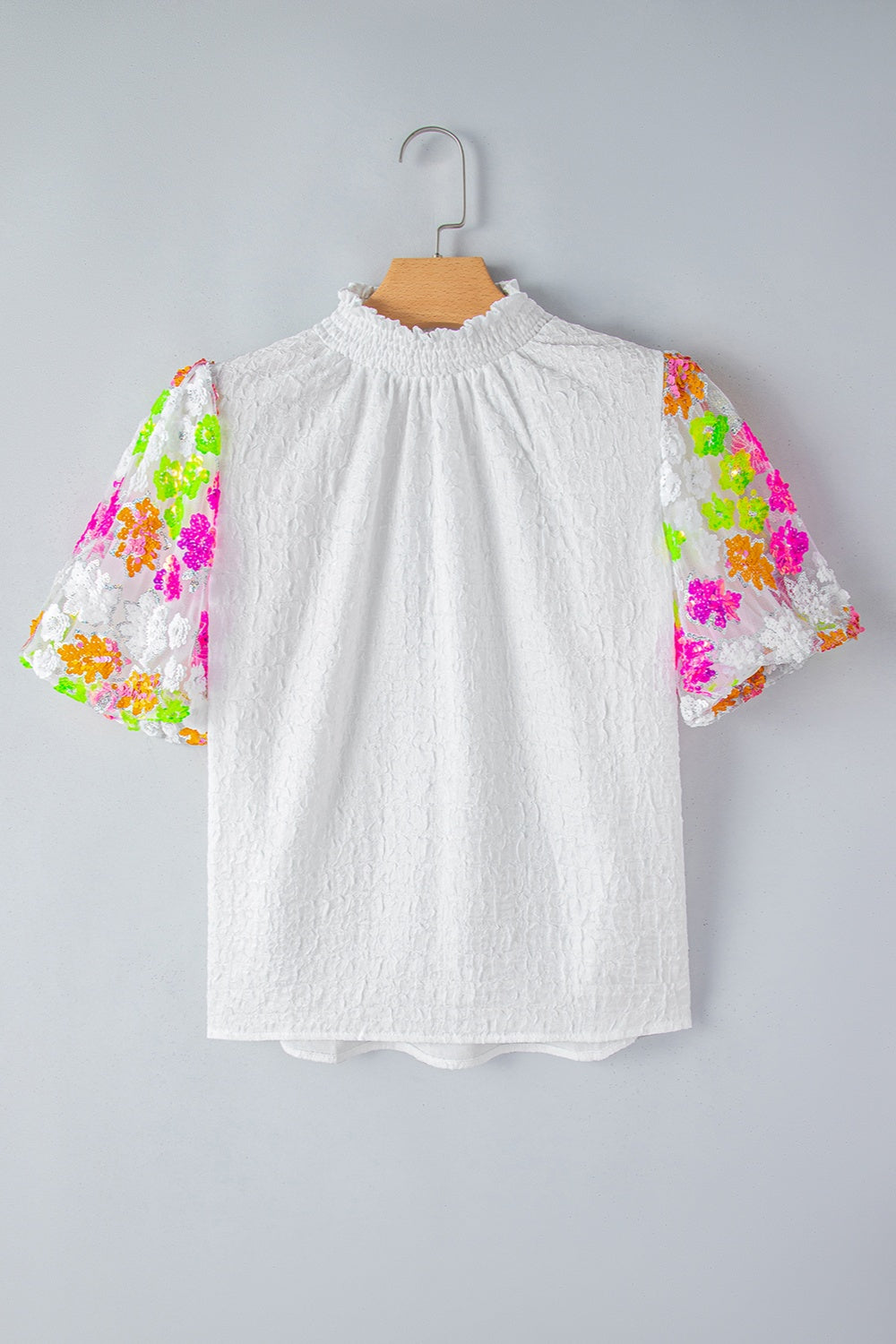White textured blouse with puff sleeves featuring colorful sequin floral embroidery and a mock neck.