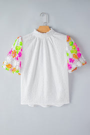 White textured blouse with puff sleeves featuring colorful sequin floral embroidery and a mock neck.