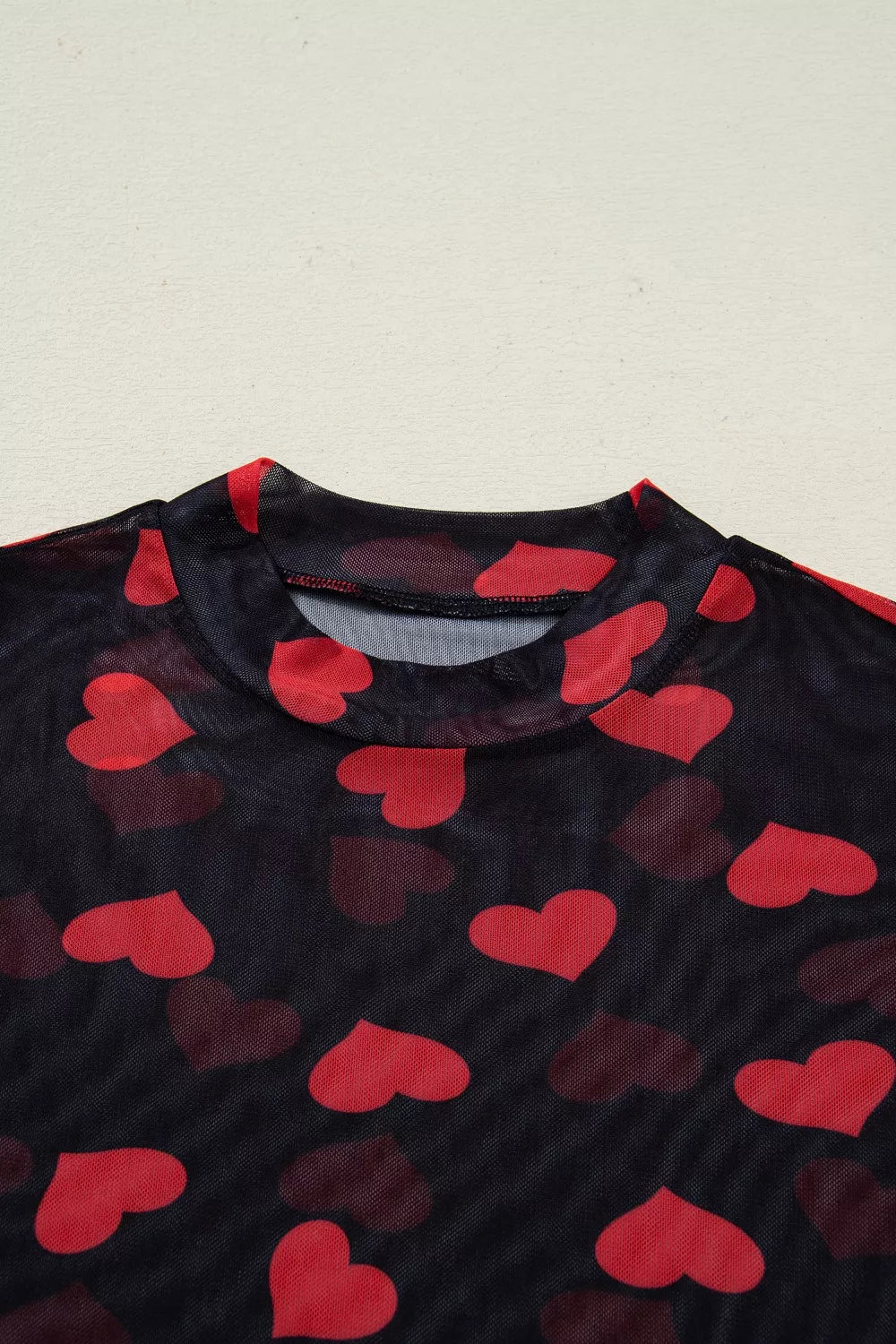 Black sheer mesh top with red heart print and mock neckline.