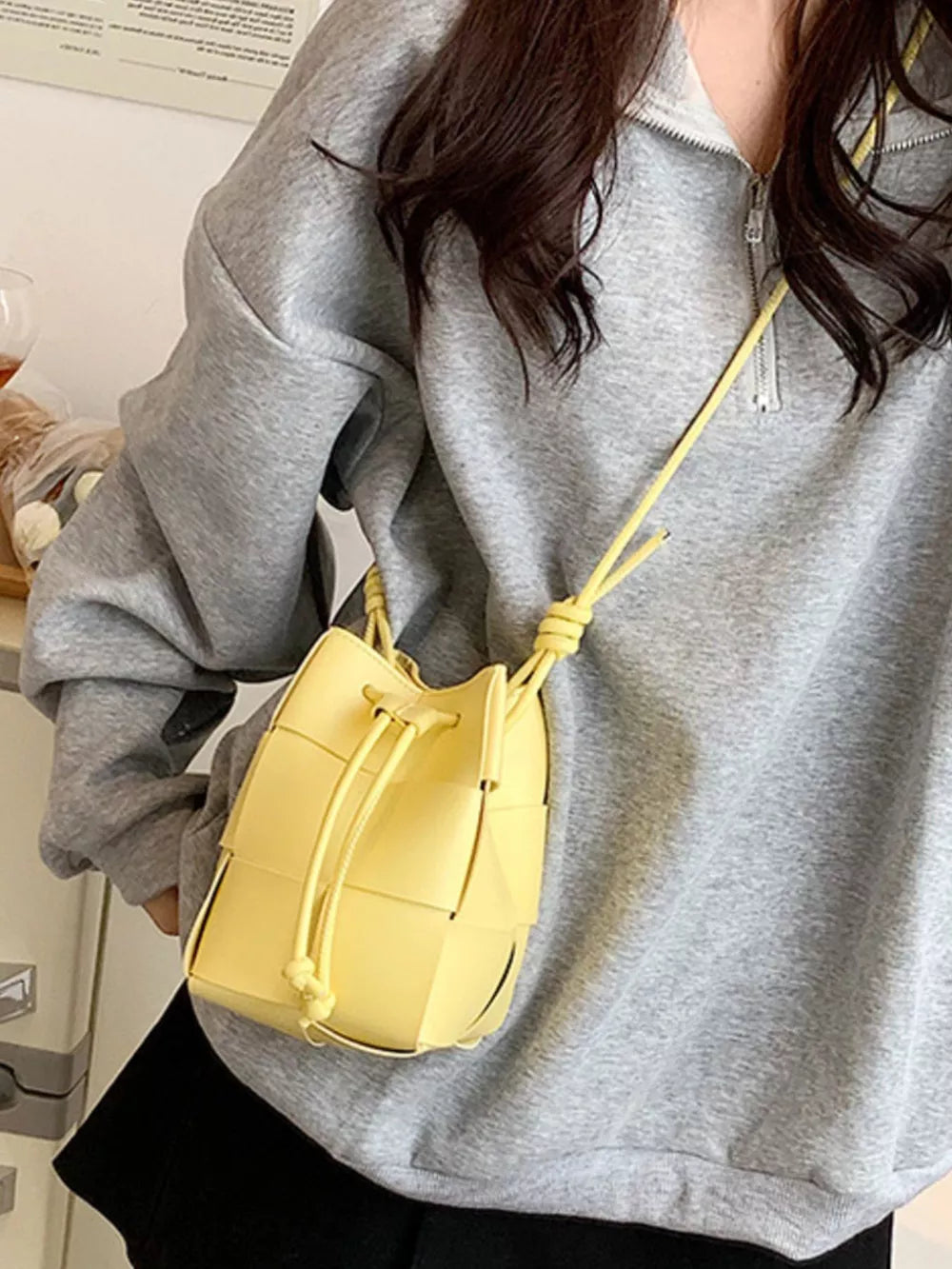 Yellow woven mini bucket bag with drawstring closure and crossbody strap.