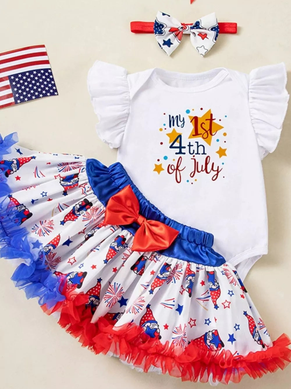 White baby onesie with "my 1st 4th of July" graphic, paired with a gnome print skirt and red bow.