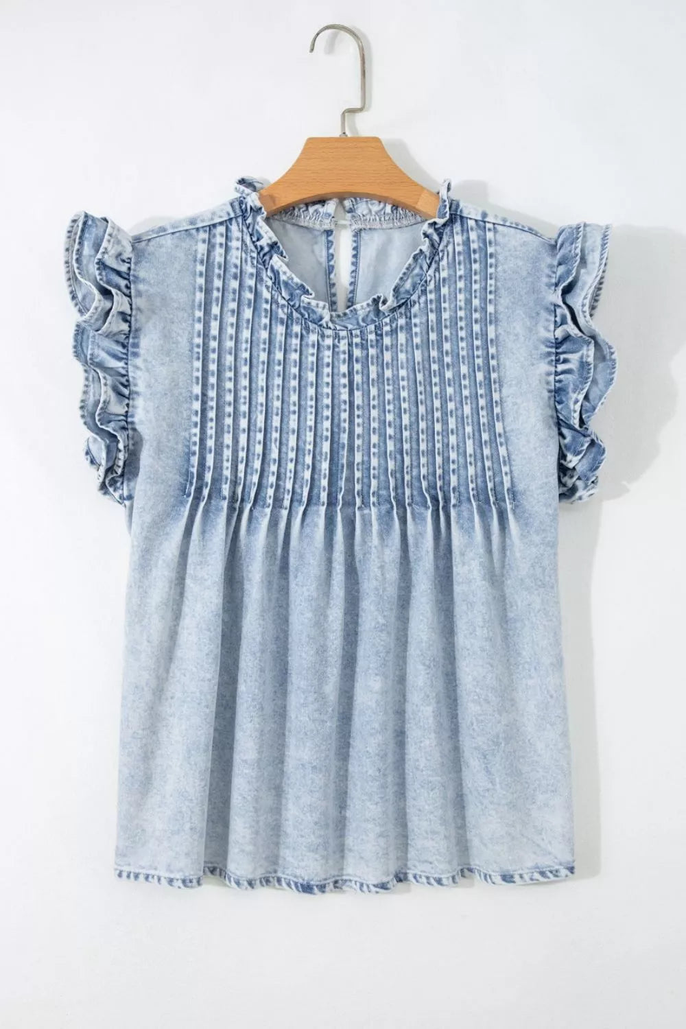 Light wash denim blouse with ruffled cap sleeves and a ruffled neckline, featuring vertical pintuck detailing.