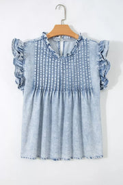 Light wash denim blouse with ruffled cap sleeves and a ruffled neckline, featuring vertical pintuck detailing.
