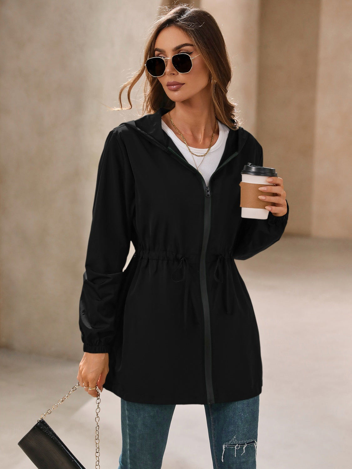 Black hooded jacket with cinched waistline and zip front, styled with jeans.
