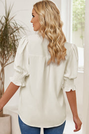 Ivory puff sleeve blouse with smocked cuffs and ruffled hem detail.