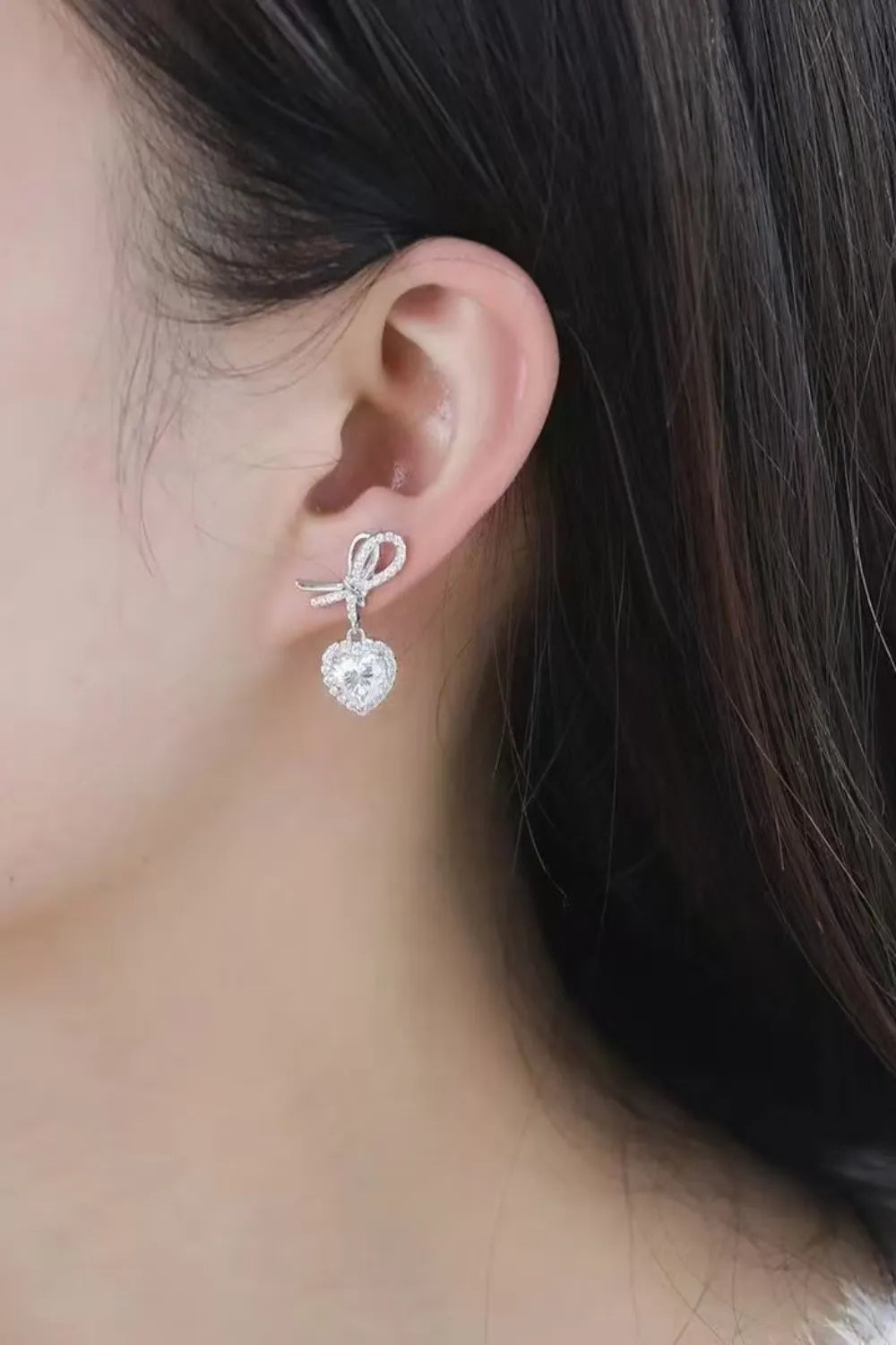 Silver bow-adorned heart moissanite drop earrings with pavé detailing.