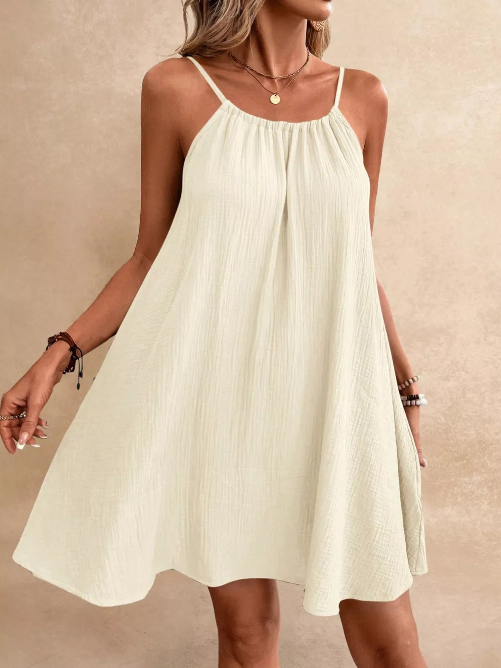 Beige spaghetti strap mini dress with gathered neckline and textured fabric.