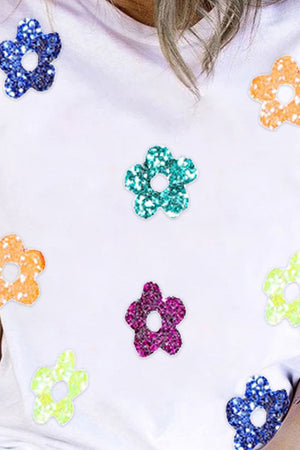 White crew neck tee with scattered glitter floral appliqués in blue, green, purple, orange, and yellow.