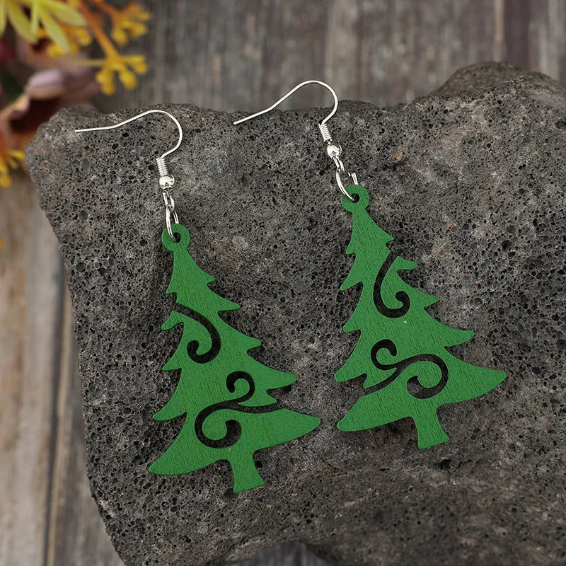 Green carved Christmas tree earrings with swirls on a dark rock.