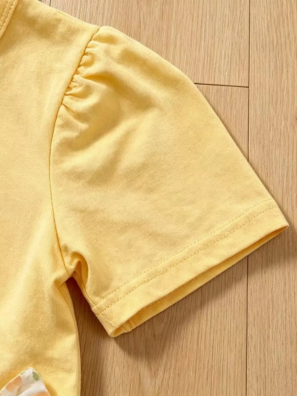 Light yellow cotton baby top with ruffled sleeves and floral pants detail.