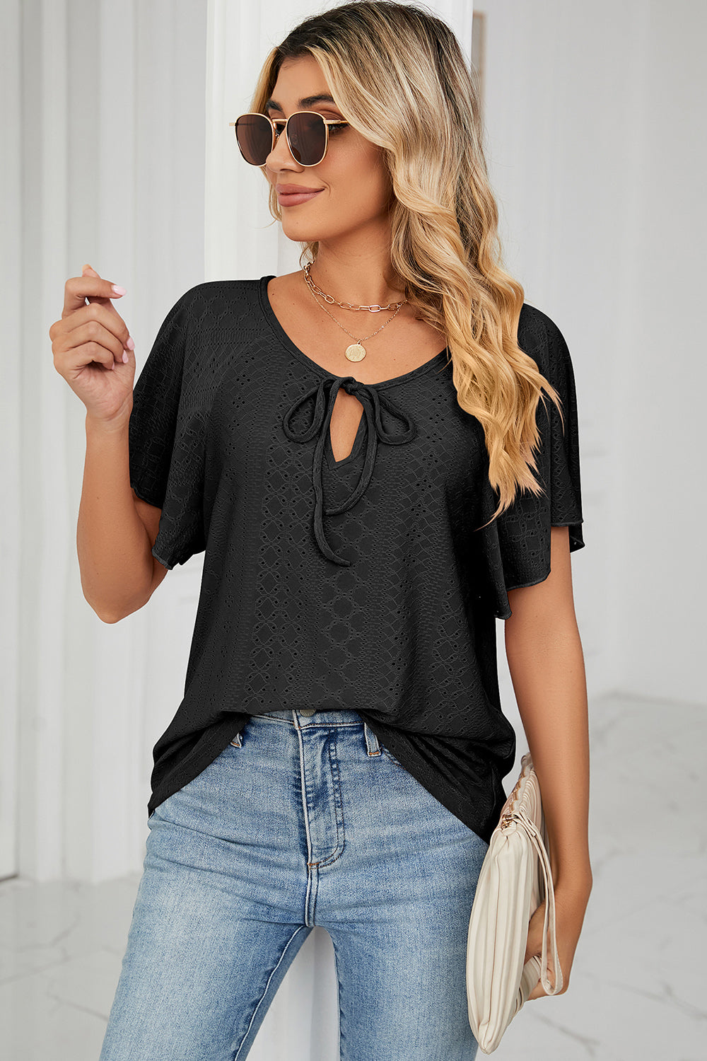 Black eyelet tie-neck blouse with flutter sleeves and a textured pattern.