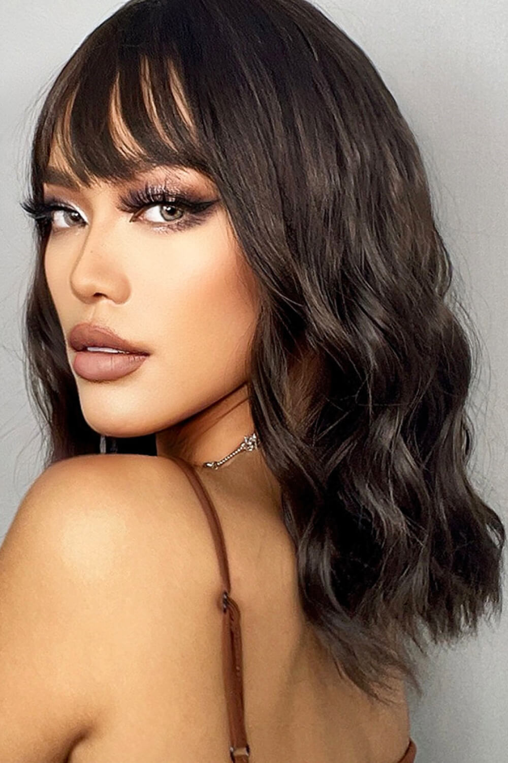 Textured black bob wig with fringe and subtle highlights, styled with soft waves.