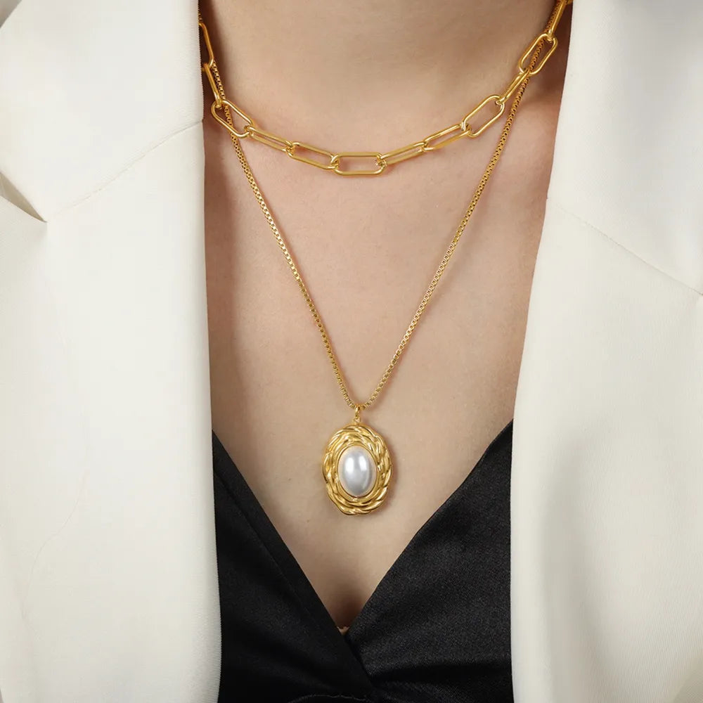 Gold double-layered necklace with oval pearl pendant and textured chain.