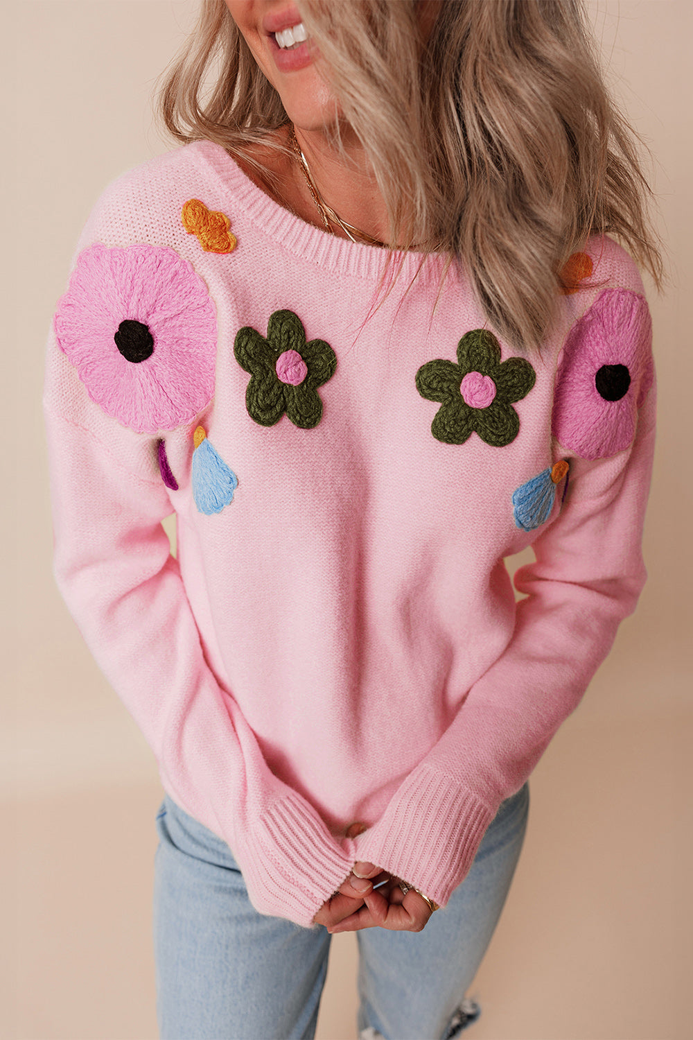 Pink knit sweater with embroidered floral appliqués and tassels.