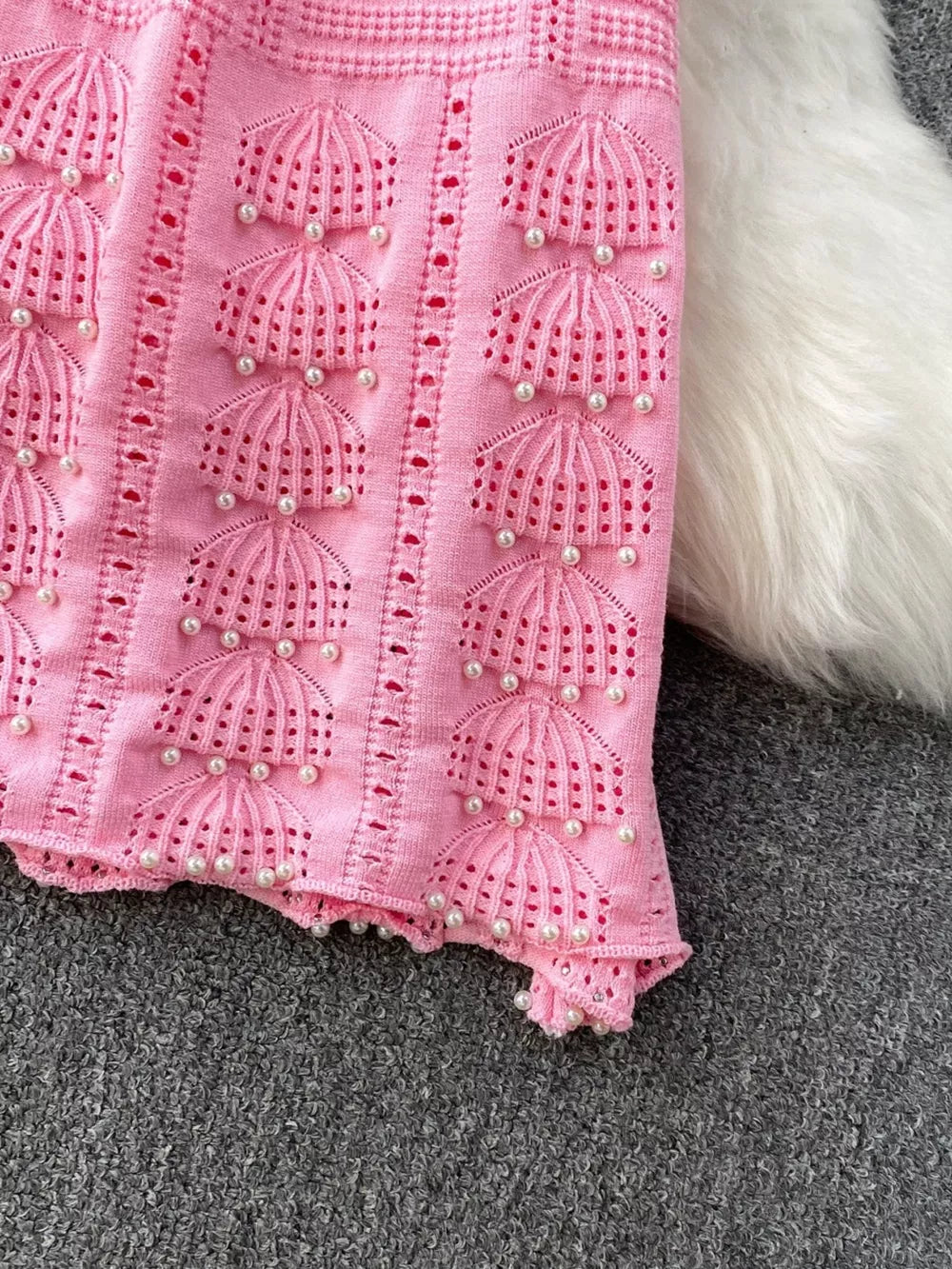 Pink knit midi dress with pearl embellishments and cutout details.
