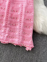 Pink knit midi dress with pearl embellishments and cutout details.