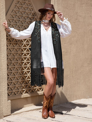 Black faux suede vest with embroidered leaf detail and fringe, styled with a white dress and cowboy boots.