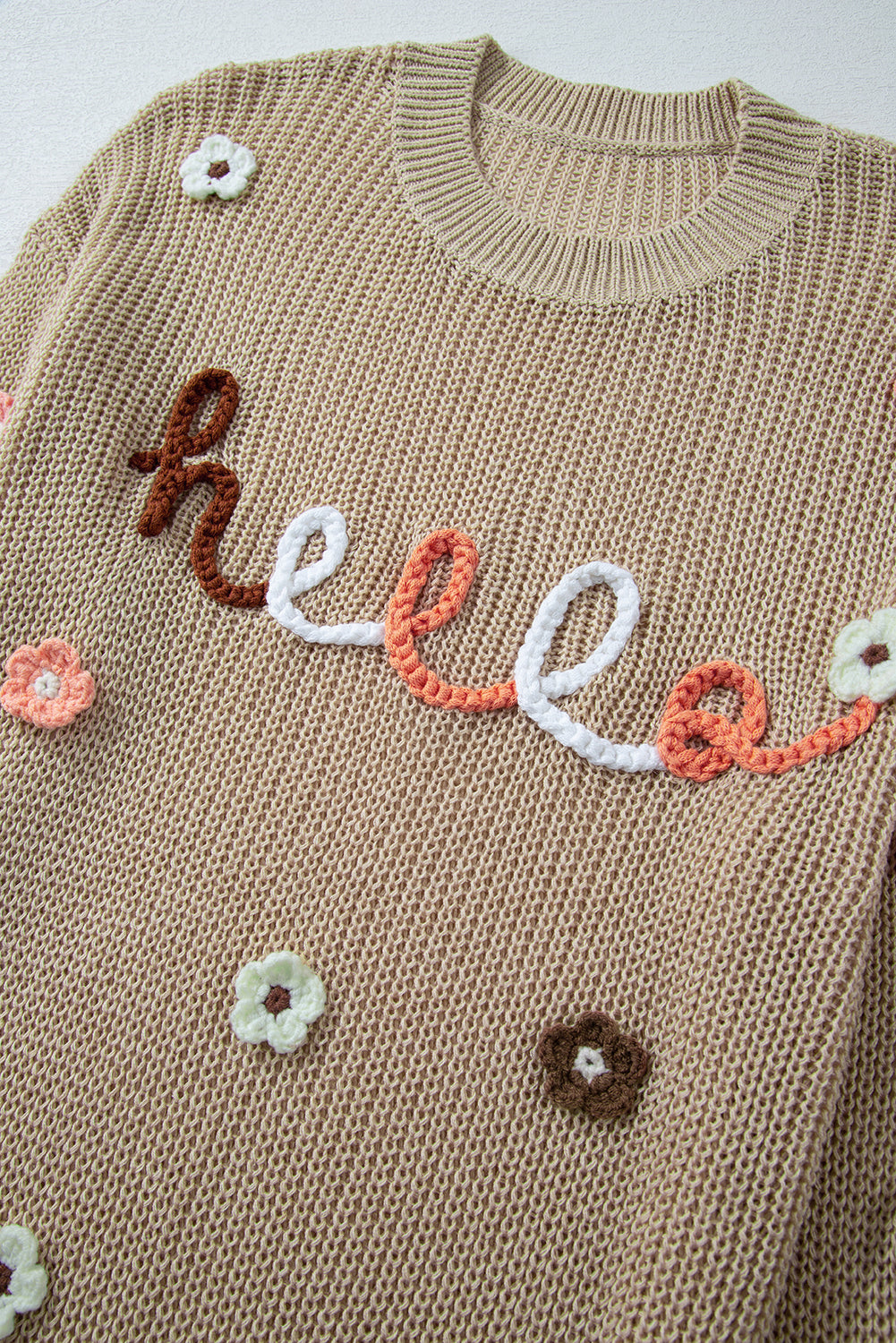 Khaki knit sweater with embroidered "hello" text and floral appliques.