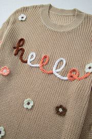 Khaki knit sweater with embroidered "hello" text and floral appliques.