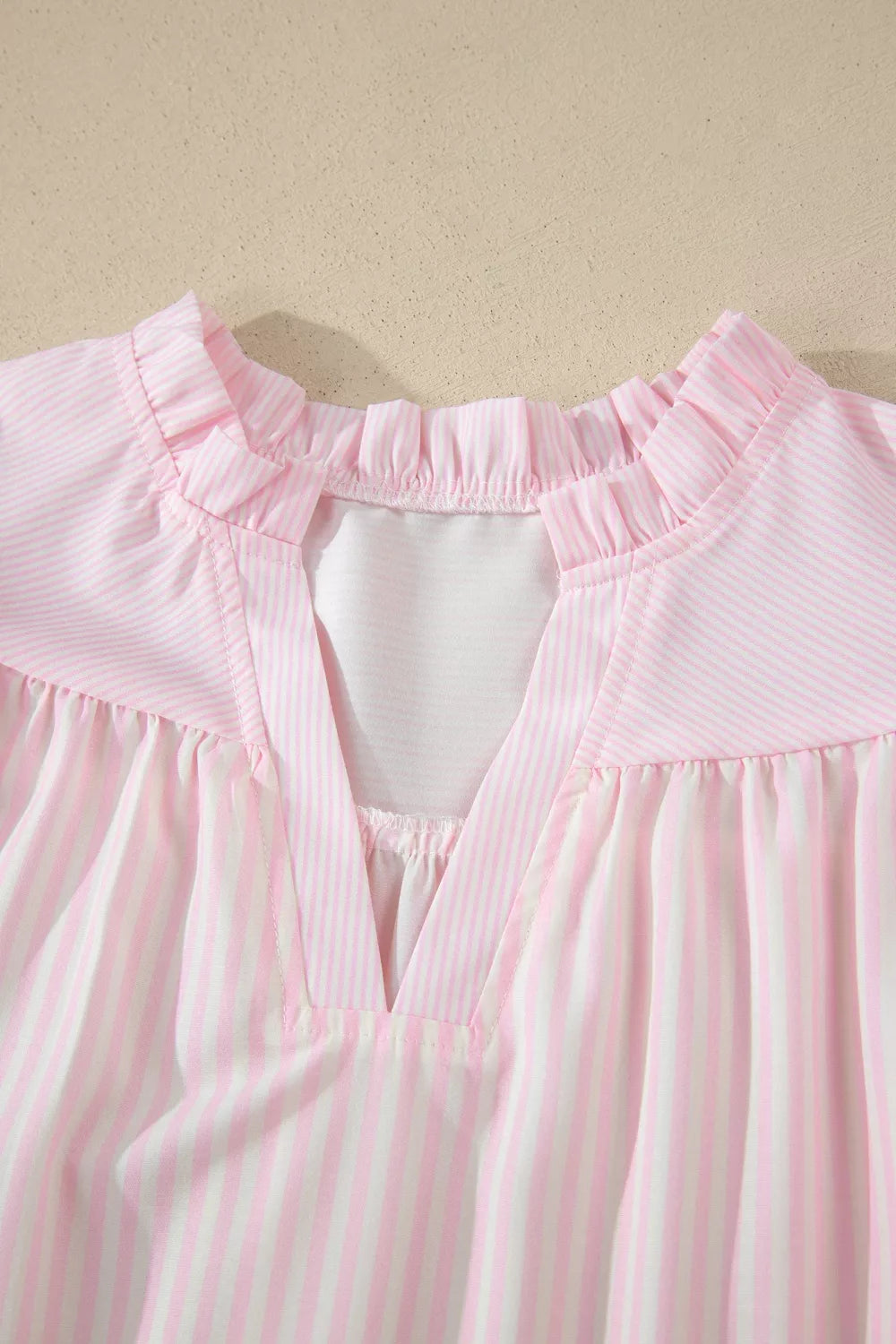 Pink and white striped polyester blouse with ruffled neckline and V-neck detail.