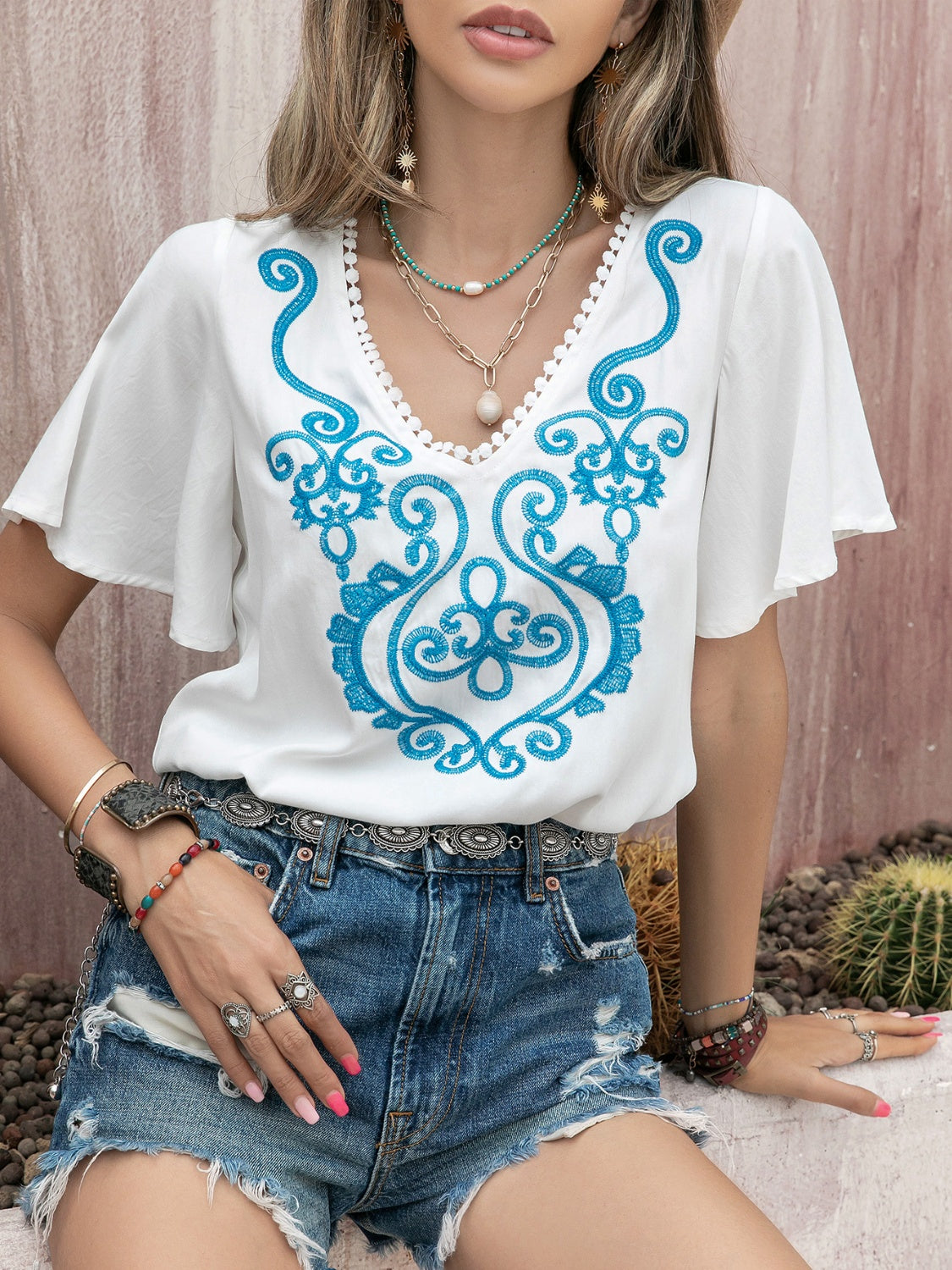 White embroidered blouse with flutter sleeves and V-neckline.