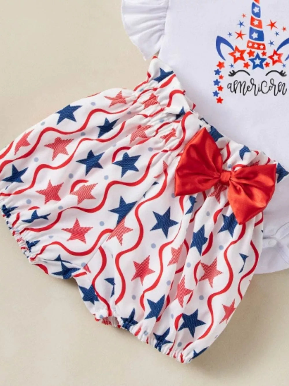 Baby outfit with white top and star print bloomer shorts, red bow detail