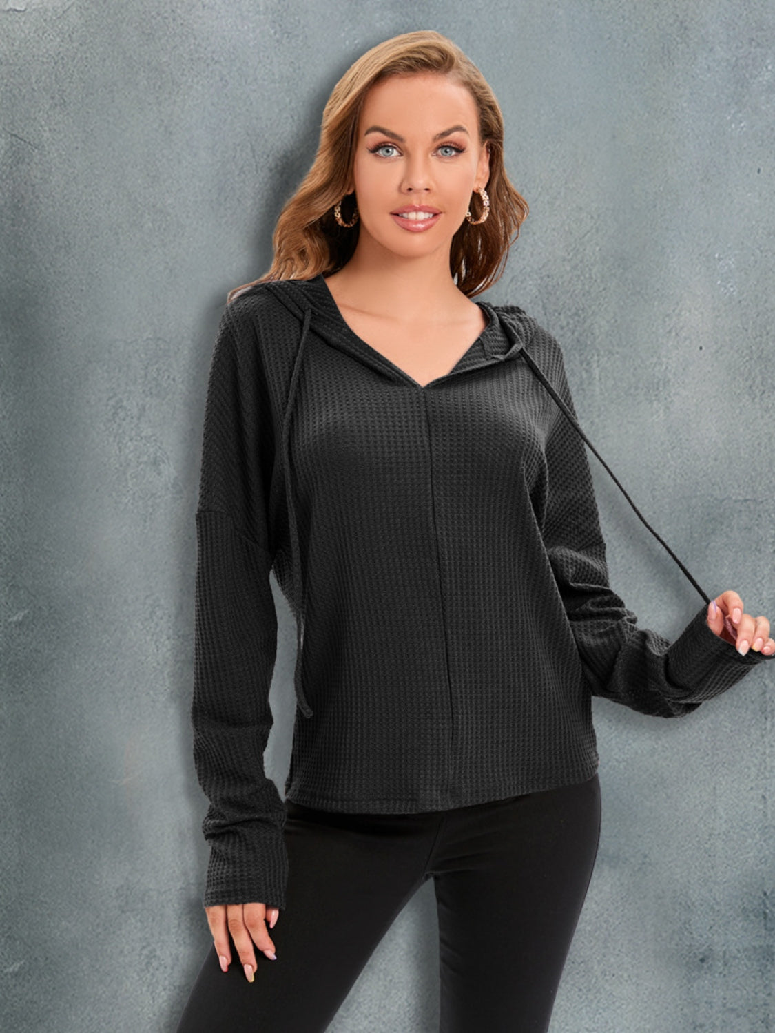 Black waffle knit hoodie with drawstring hood and relaxed fit.