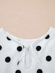 White polka dot blouse with tie-neck detail and smocked cuffs.