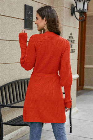 Orange-red knit cardigan with puffed sleeves and a belted waist.