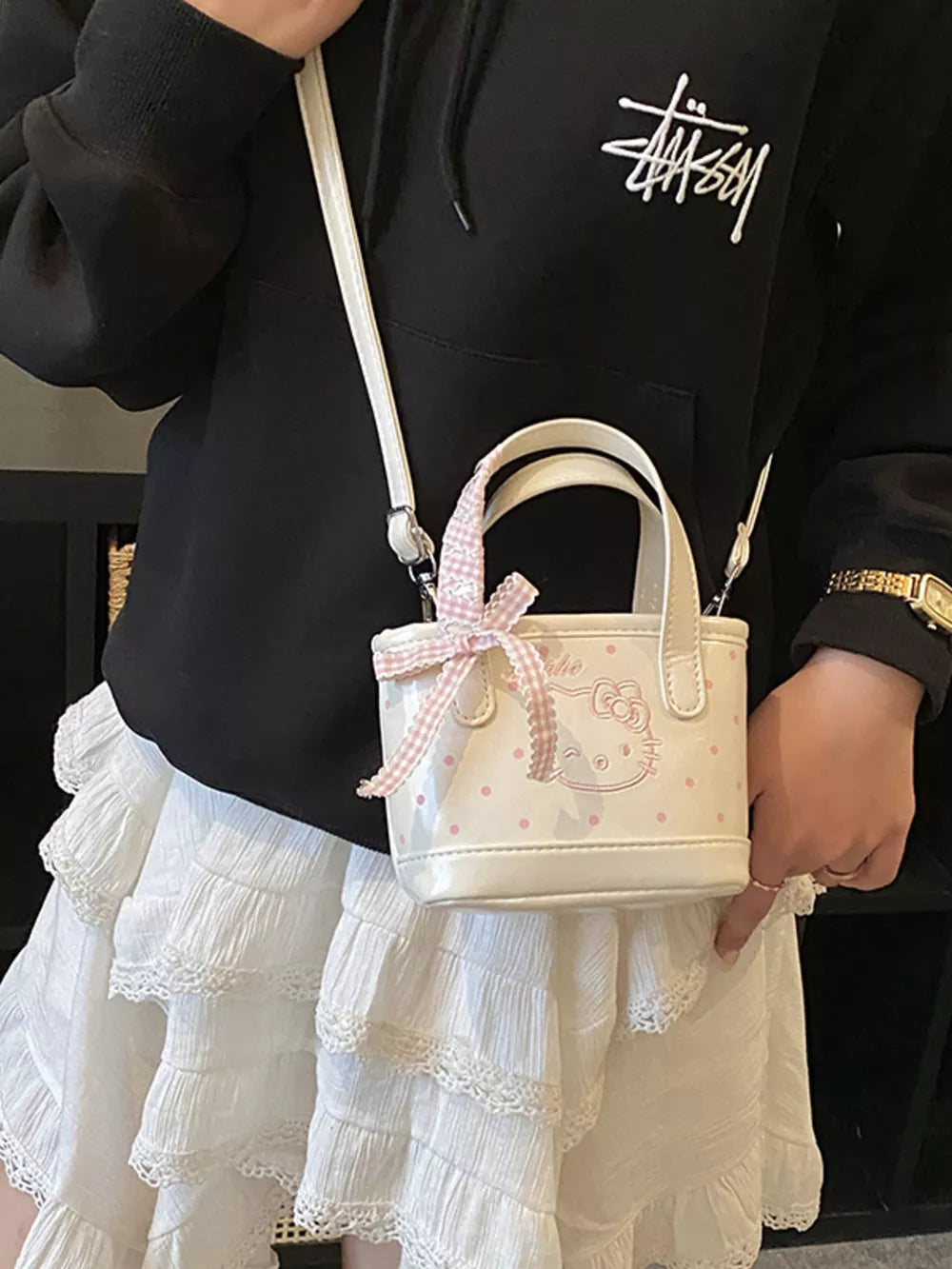 Charming mini crossbody bag in white with pink polka dots and Hello Kitty graphic, tied with a pink gingham bow.