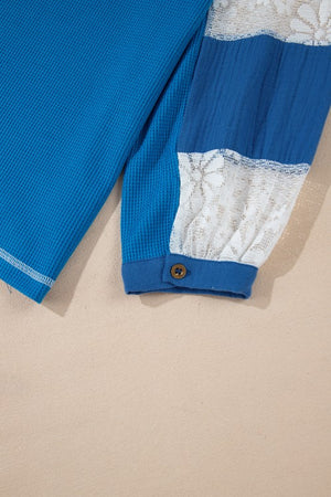 Blue waffle knit top with white lace paneled sleeves and button cuff detail.