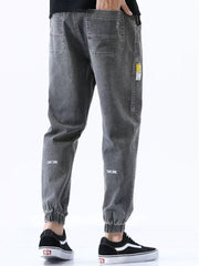 Men's grey relaxed fit drawstring jeans with elastic cuffs and subtle leg embroidery.