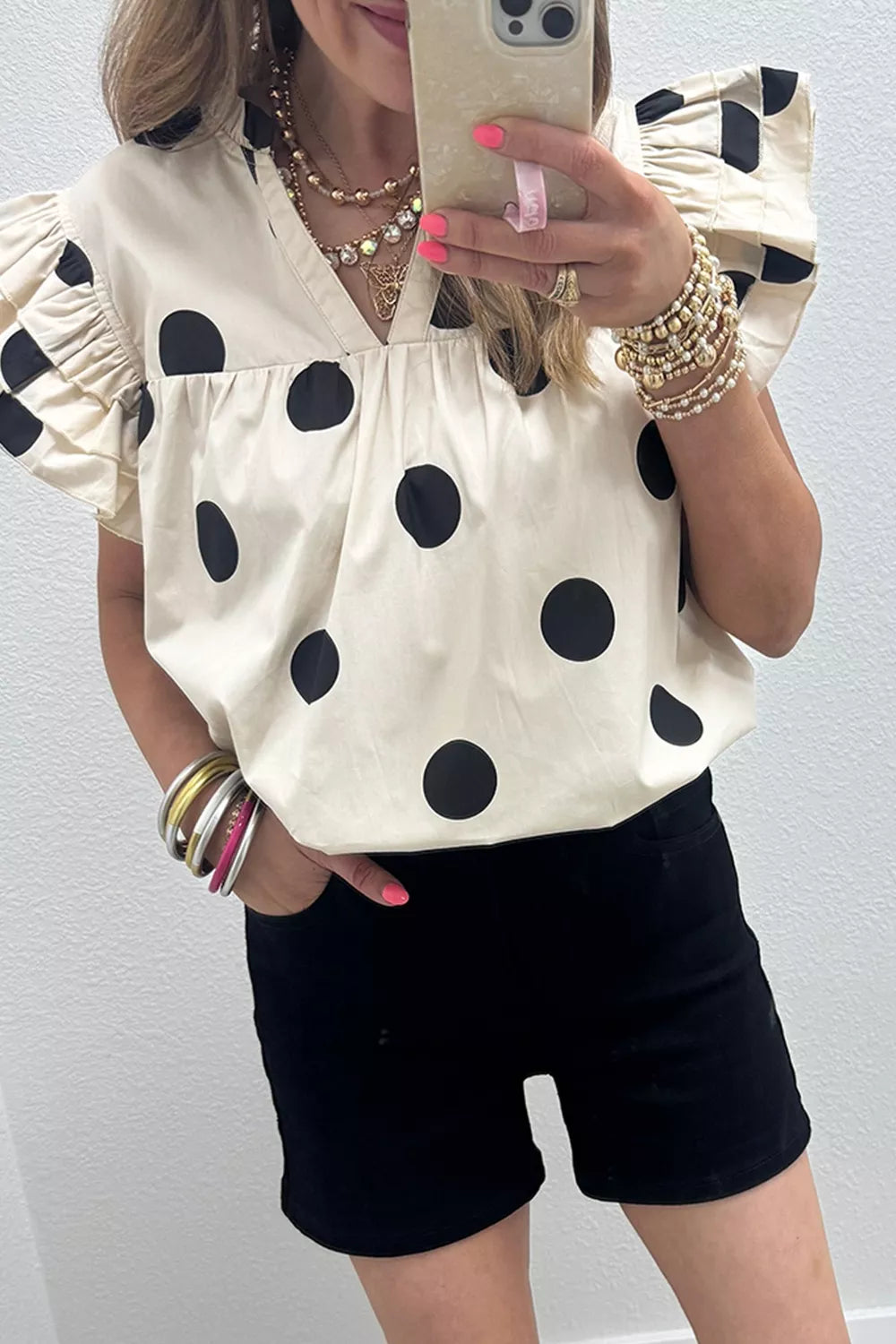Cream cotton v-neck shirt with black polka dots and ruffled short sleeves.