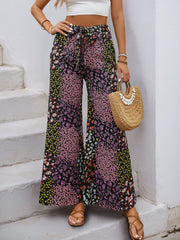 Floral panel palazzo trousers in black with a tie waist and wide leg, styled with a white crop top and sandals.