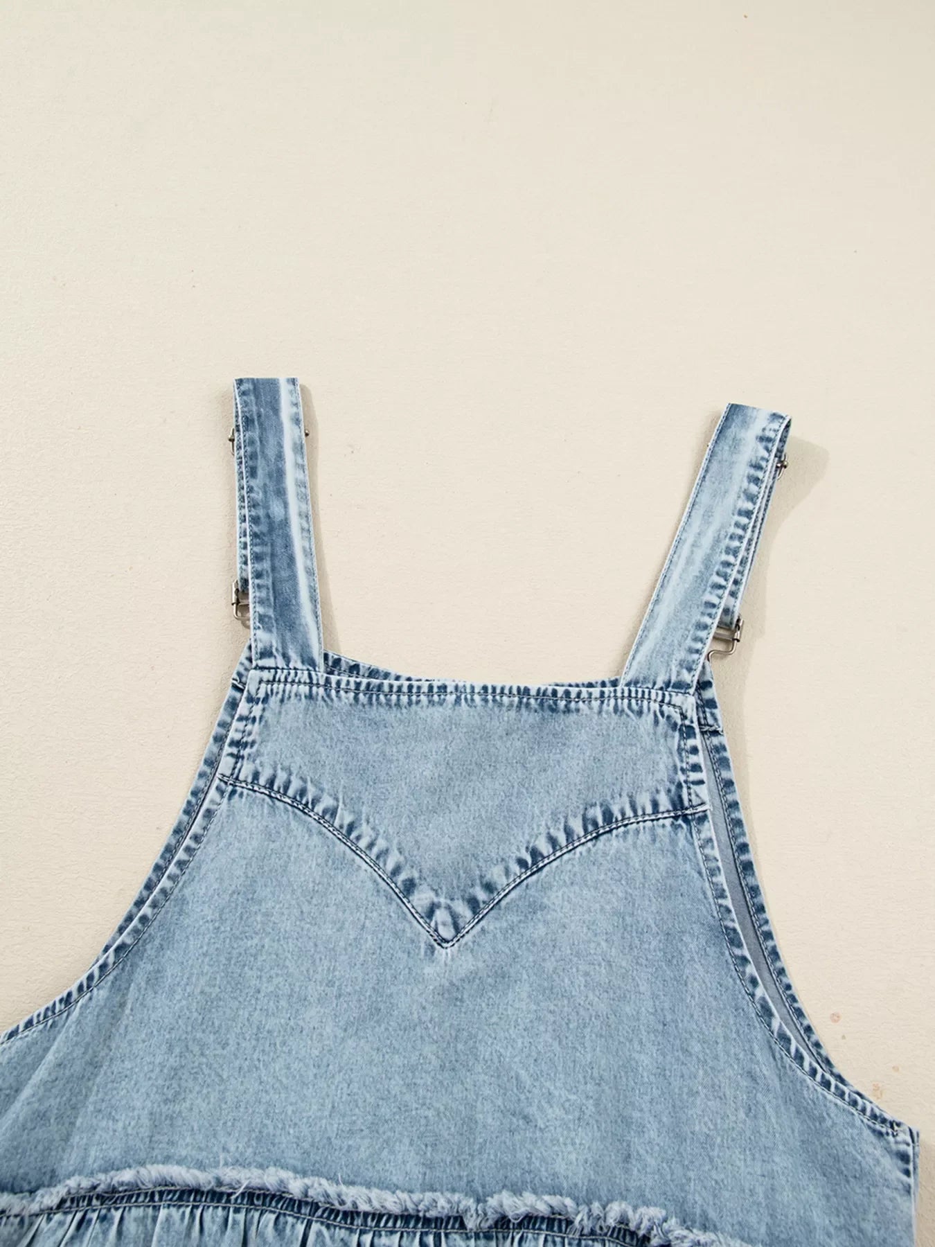 Tiered denim overall dress in light blue with adjustable straps and frayed hem detail.