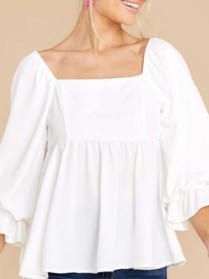 White babydoll blouse with square neckline, puff sleeves, and ruffled cuffs.