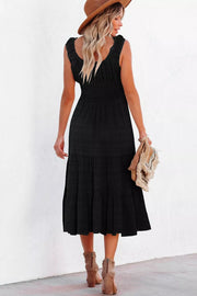 Black smocked tiered midi dress with ruffled neckline and pockets, styled with a hat and clutch.