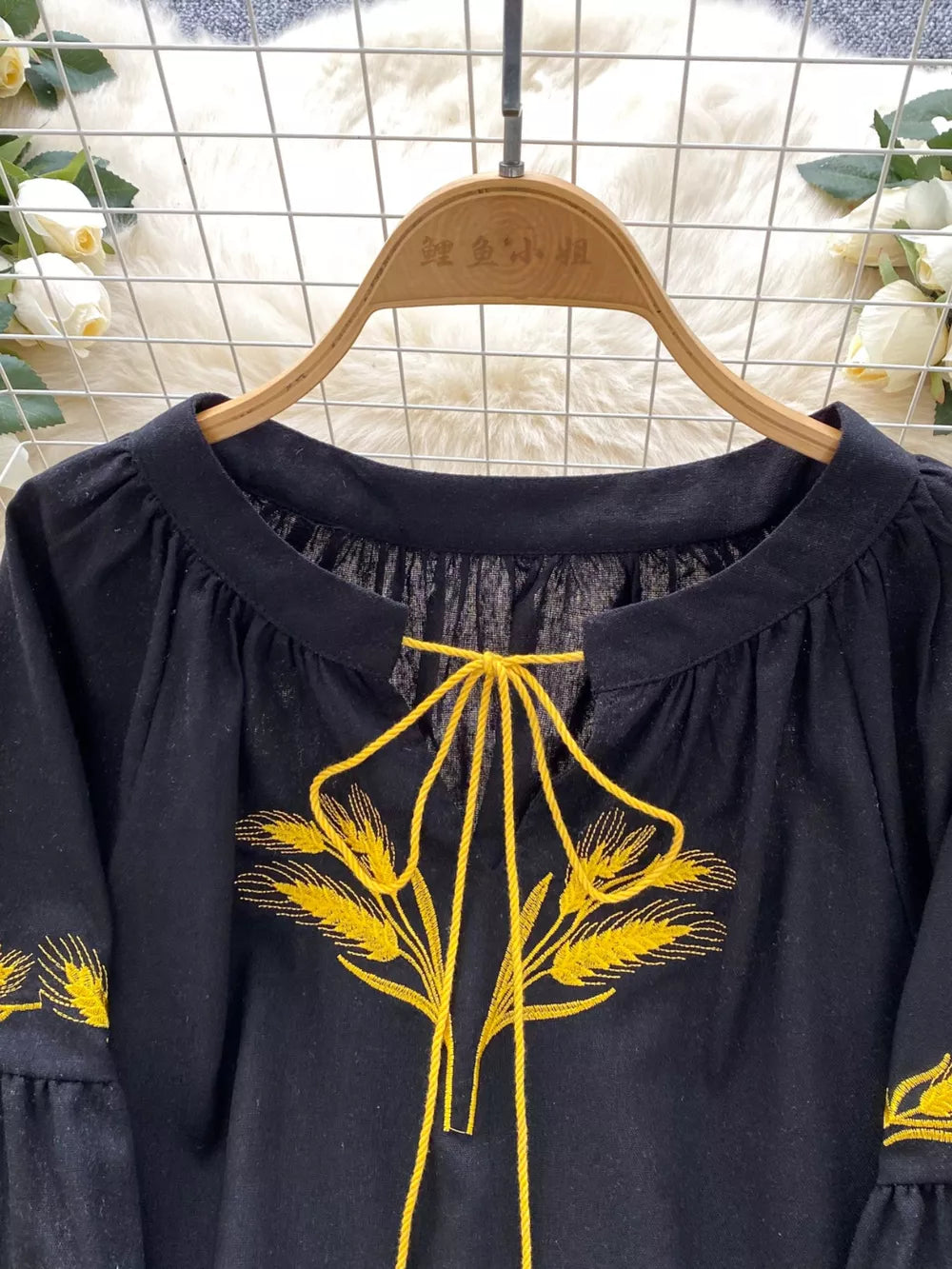 Black tie-neck blouse with yellow wheat embroidery and bell sleeves.
