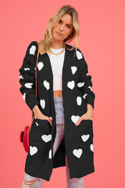Black longline knit cardigan with white heart motif, featuring pockets and a relaxed fit.