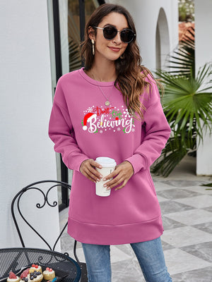 Pink graphic tunic sweatshirt with "Don't Stop Believing" holiday print and Santa hat detail.