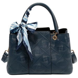 Elegant geometric embossed tote handbag in blue with a decorative scarf tied to the handle.