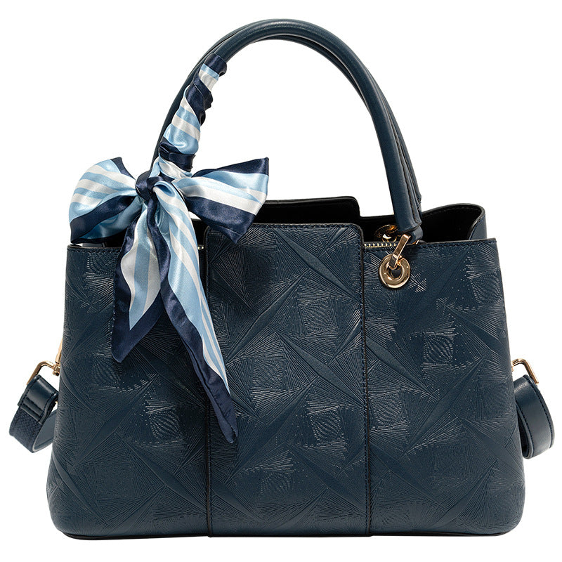 Elegant geometric embossed tote handbag in blue with a decorative scarf tied to the handle.