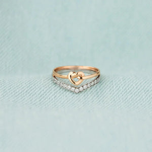 Stacking rings with a gold heart knot and a chevron band of cubic zirconia on a light blue textured background.