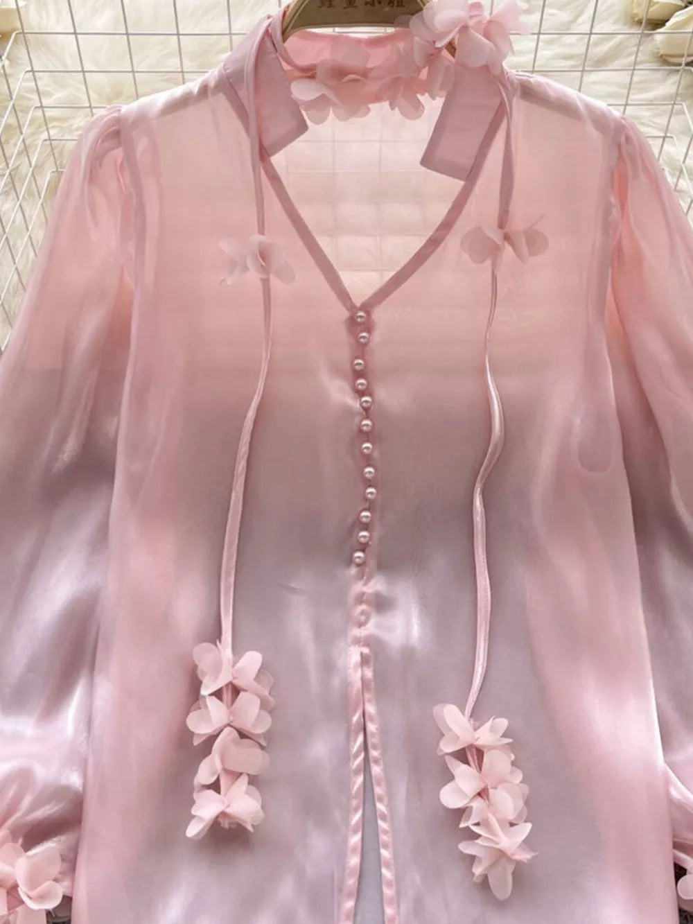 Pink sheer organza shirt with floral appliqué and pearl buttons.