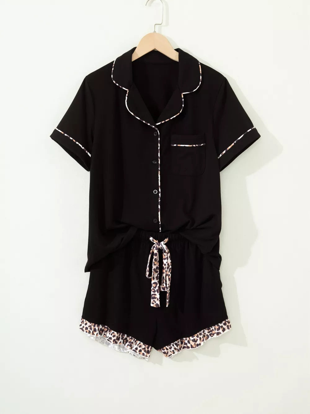 Black button-up pajama set with leopard trim on collar, cuffs, pocket, shorts tie and hem.