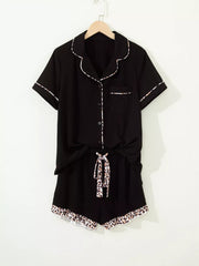 Black button-up pajama set with leopard trim on collar, cuffs, pocket, shorts tie and hem.